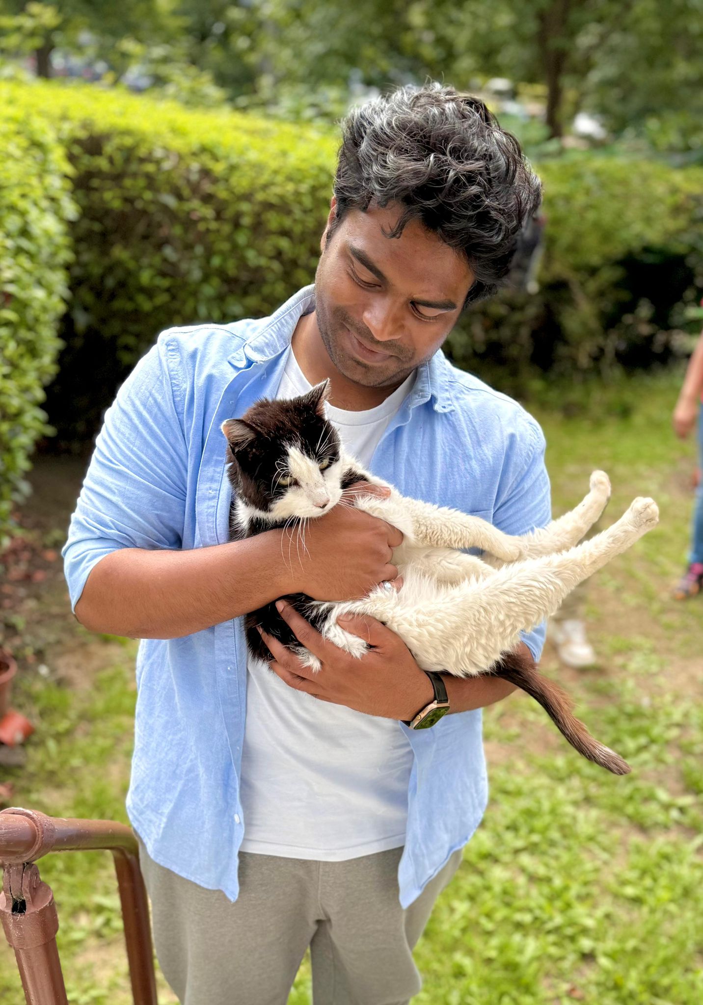 Virendra smiling down at a black-and-white cat he is holding outdoors